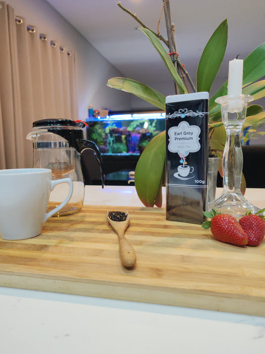 Tea-making setup with a bottle of Earl Grey tea, strawberries, and a wooden spoon on a wooden board.