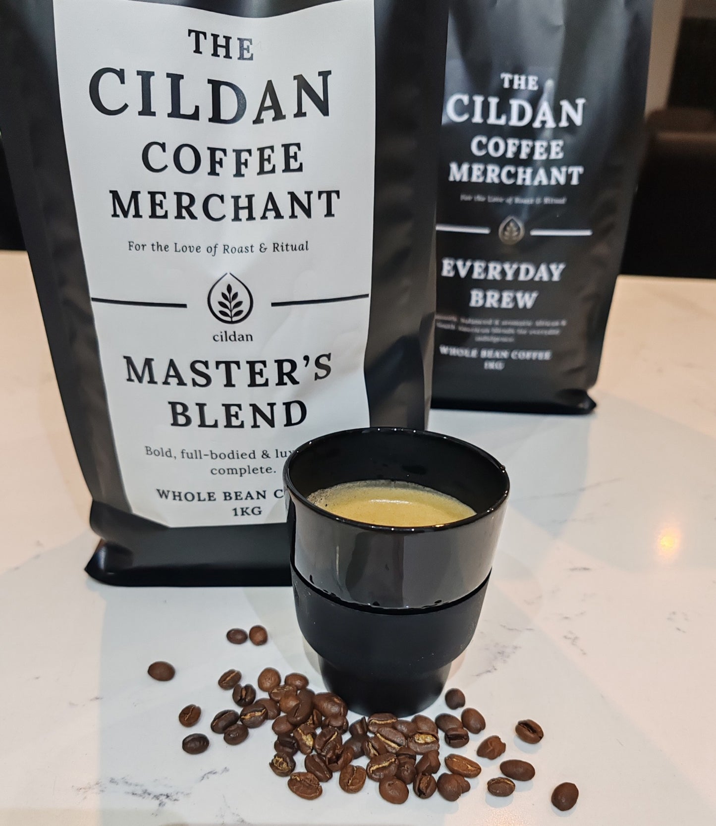 Cildan Coffee Merchant coffee bags with a cup of coffee and coffee beans on a marble surface.