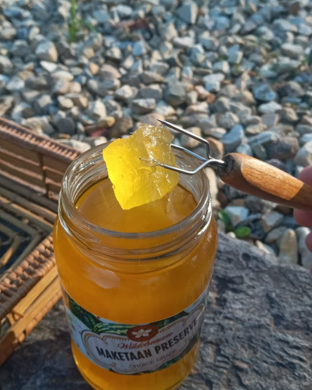 Jar of preserve with a spoonful being lifted, against a gravel background