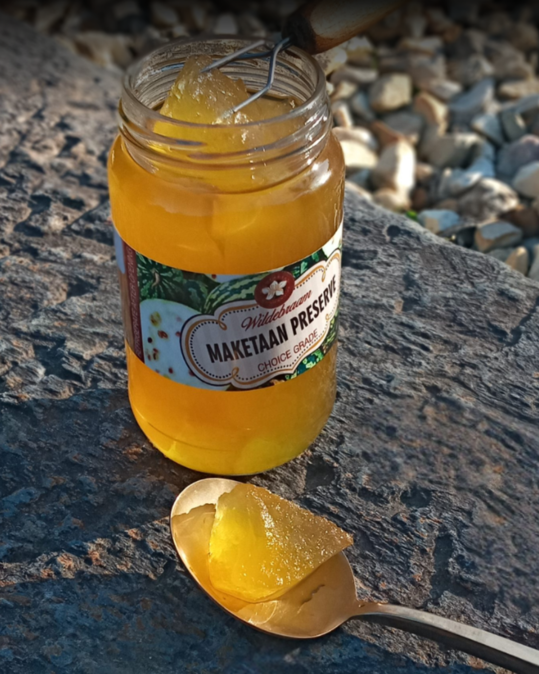 Jar of Maketaan Preserves with a spoonful of preserve on a stone surface