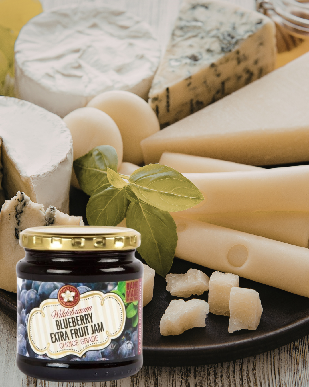 Jar of blueberry jam on a plate with assorted cheeses