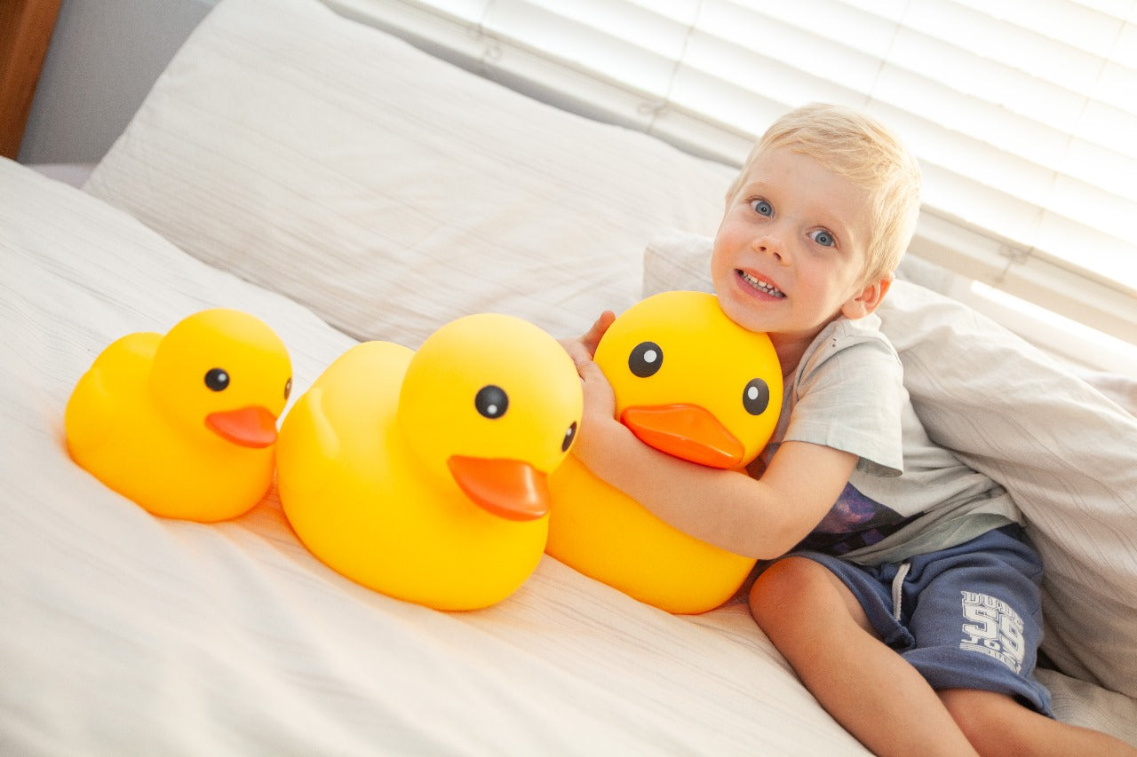 Child holding a large yellow rubber duck on a bed
