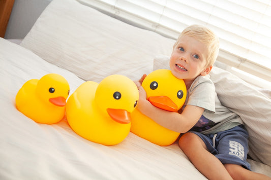 Child holding a large yellow rubber duck on a bed