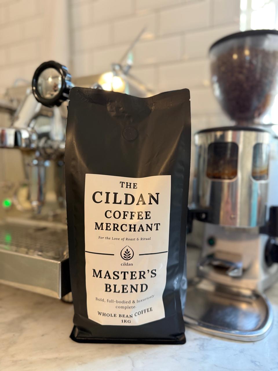 Bag of The Cildan Coffee Merchant Master's Blend coffee on a kitchen counter with coffee-making equipment in the background.