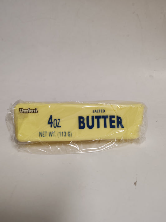A 4 oz stick of Umnofi Salted Butter in its clear plastic wrapper, showing the yellow butter inside and blue text, placed on a plain off-white surface.