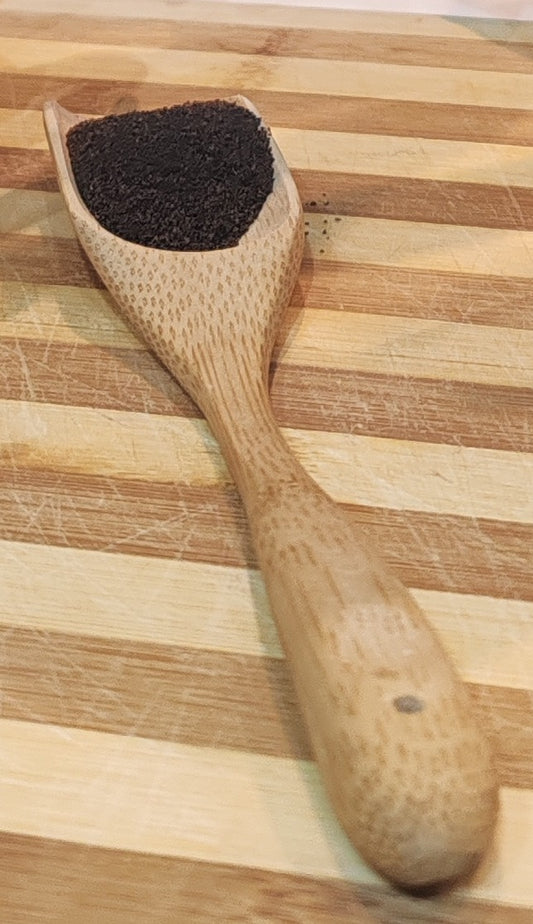 Wooden scoop filled with dark Kenyan Tea on a wooden surface