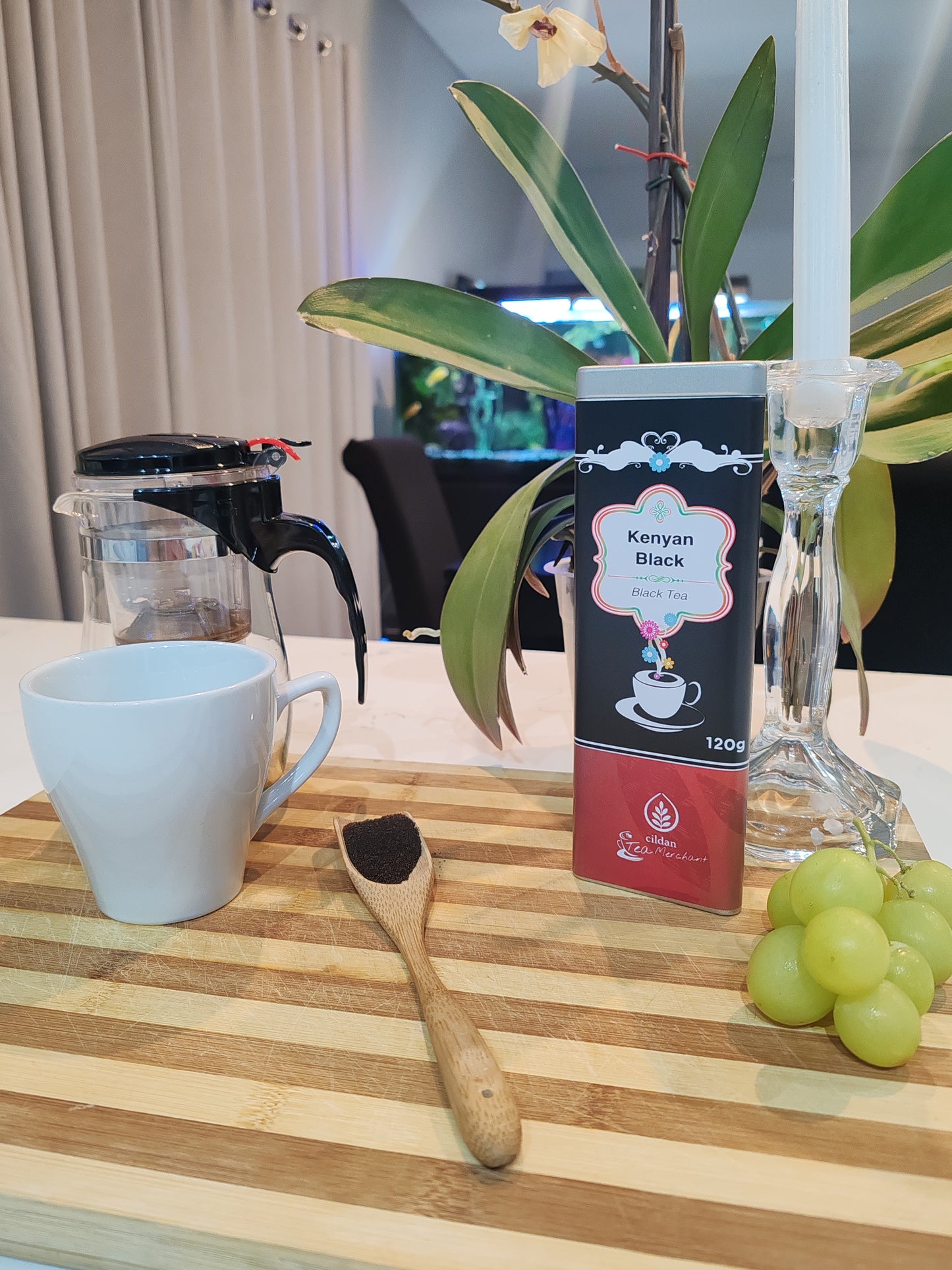 Tea Pot, mug, spoon, grapes, and plant on a wooden surface
