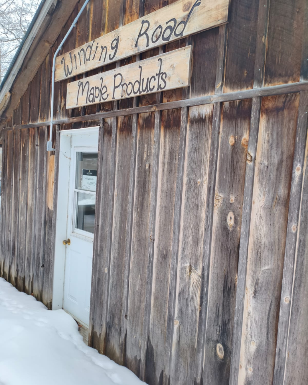 Wooden building with 'Winding Road Maple Products' sign in a snowy setting