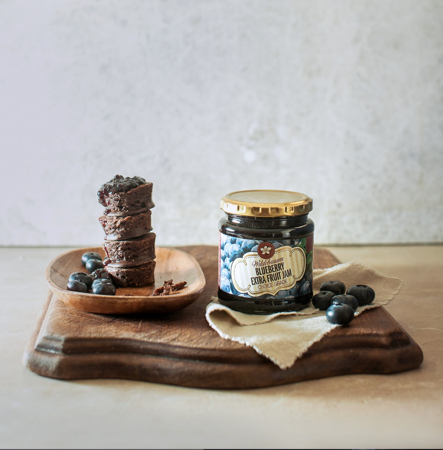 Jar of blueberry jam with a dessert and blueberries on a wooden board.